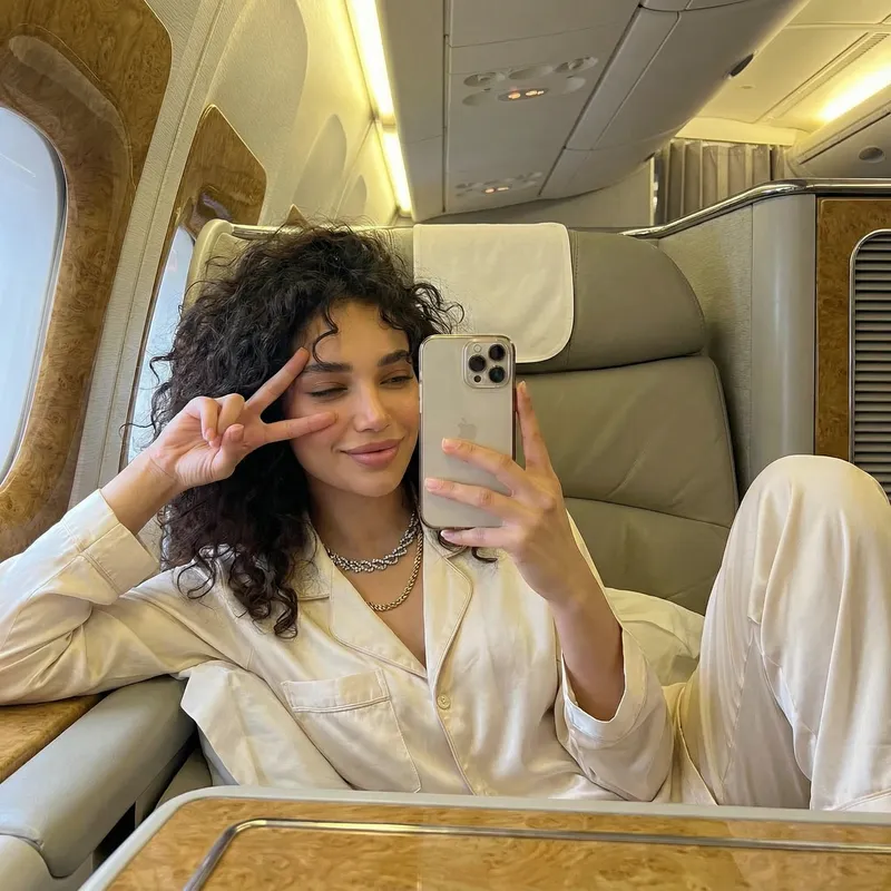 A woman snaps a front-facing selfie while reclining with her…